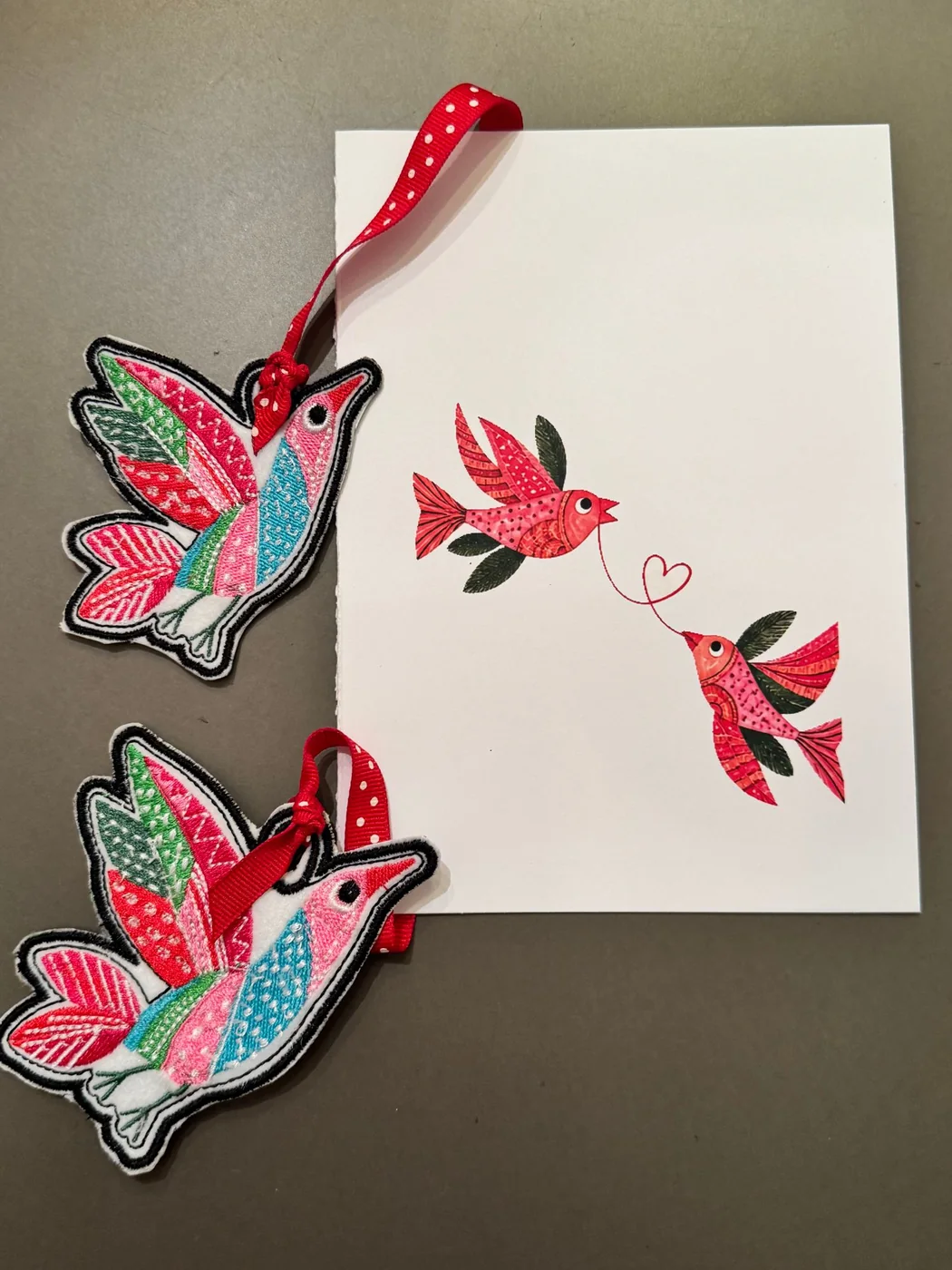 An embroidered bird bookmark beside the Woven Together card