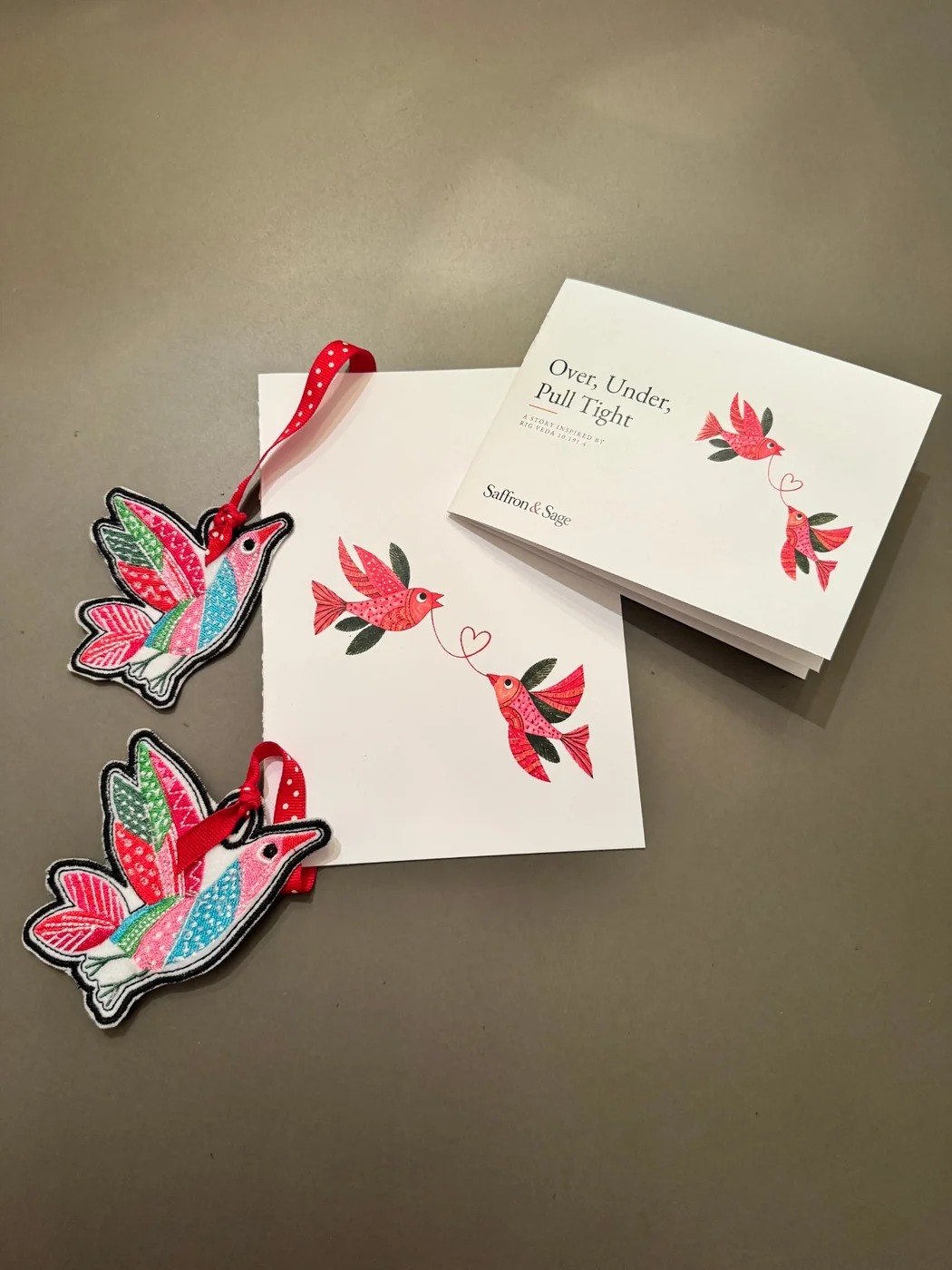 Woven Together gift kit: the card, the story booklet Over, Under, Pull Tight, and an embroidered bookmark with a bird at each end of a red polka-dot ribbon